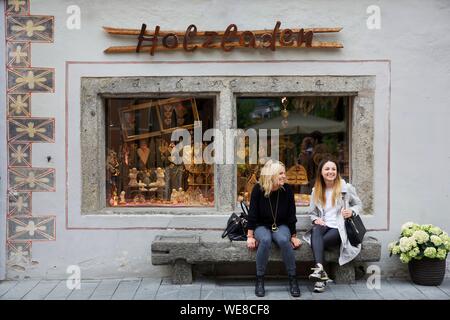 Italy, autonomous province of Bolzano, Brunico, two women sitting on a stone bench in front of a craft shop in a downtown alley Stock Photo