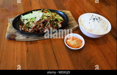 Grilled pork neck with barbecue sauce (Tontoro) with fried vegetables in a black plate, Japanese food with steamed rice and kimchee on brown table Stock Photo