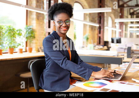 Interior designer smiling while typing e-mail for client Stock Photo