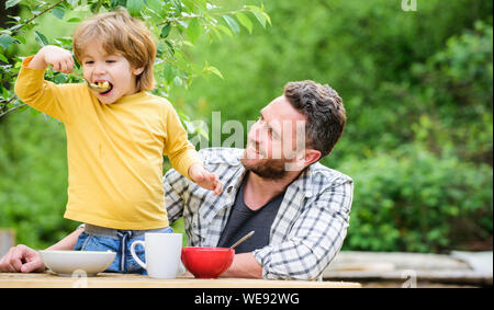 Food habits. Little boy with dad eating food picnic yard nature background. Summer breakfast. Healthy food concept. Father son eat food and have fun. Menu for children. Family enjoy homemade meal. Stock Photo