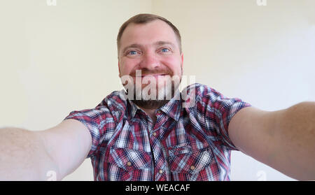 Selfie portrait! Handsome bearded man taking selfie photo and smiling on the light background. Stock Photo
