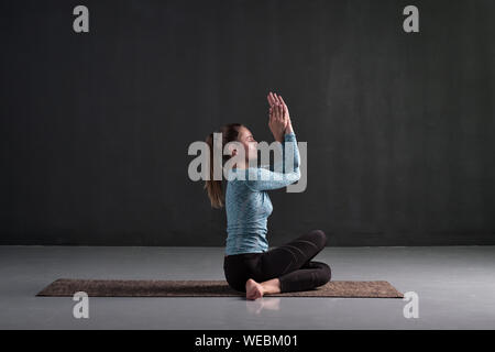 Young woman sitting in Gomukhasana, Cowface pose variation. Studio full length shot Stock Photo