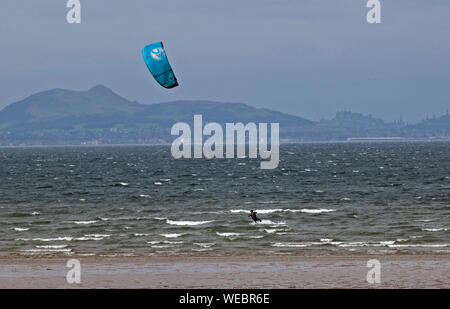 Longniddry Bents, East Lothian, Scotland, UK. 30th Aug, 2019. One solitary Kite Surfer out Kiteboarding braves the choppy Firth of Forth and gusty wind at Longniddry where dull dreary conditions gave way to a brightening sky by noon, with Edinburgh Castle and Arthur's Seat in the background. Estimated Wind: 42 km/h SW. Gusts: 63 km/h. Stock Photo