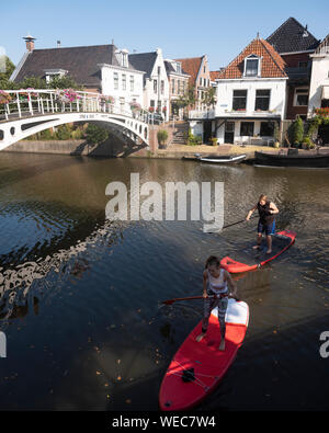 girls on surf boards paddle in canal of old town dokkum in dutch province of friesland Stock Photo