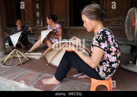 (190830) -- HANOI, Aug. 30, 2019 (Xinhua) -- Local women make traditional conical hats in the Chuong village on the outskirts of Hanoi, capital of Vietnam on Aug. 29, 2019. Vietnam's traditional conical hats are mostly made from bamboo and palm leaves, and they are among the country's most impressive traditional costumes. People in the Chuong village have been making conical hats for about 400 years. The locals buy green palm leaves from other provinces, dry them in the sun and iron and bleach the leaves into flat slices. They then use thin strings to fix layers of leaves on a cone made of bam Stock Photo