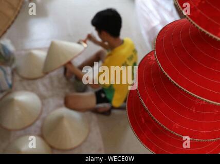 (190830) -- HANOI, Aug. 30, 2019 (Xinhua) -- A local young man makes traditional conical hats in the Chuong village on the outskirts of Hanoi, capital of Vietnam on Aug. 29, 2019. Vietnam's traditional conical hats are mostly made from bamboo and palm leaves, and they are among the country's most impressive traditional costumes. People in the Chuong village have been making conical hats for about 400 years. The locals buy green palm leaves from other provinces, dry them in the sun and iron and bleach the leaves into flat slices. They then use thin strings to fix layers of leaves on a cone made Stock Photo