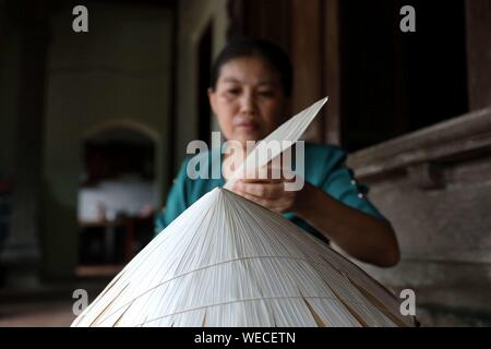 (190830) -- HANOI, Aug. 30, 2019 (Xinhua) -- A woman fixes palm leaves onto a bamboo cone to make a traditional conical hat in the Chuong village on the outskirts of Hanoi, capital of Vietnam on Aug. 29, 2019. Vietnam's traditional conical hats are mostly made from bamboo and palm leaves, and they are among the country's most impressive traditional costumes. People in the Chuong village have been making conical hats for about 400 years. The locals buy green palm leaves from other provinces, dry them in the sun and iron and bleach the leaves into flat slices. They then use thin strings to fix l Stock Photo
