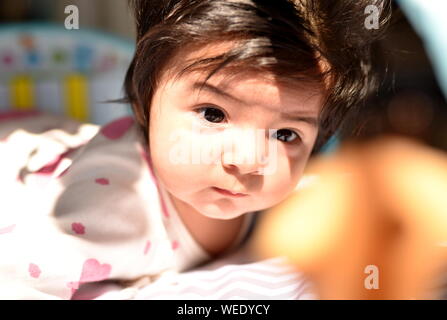 Cute mixed race baby girl looks attentively at her toys in nursery Stock Photo