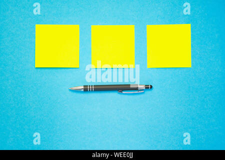 three yellow adhesive labels in a row over a pen against blue background, copy space Stock Photo