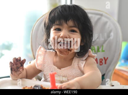 Cute happy baby girl messy eating birthday chocolate cake Stock Photo