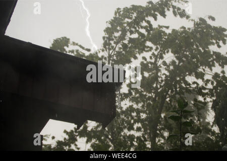 Heavy rain and lighting in the garden. House with water poured from the gutter. Stock Photo