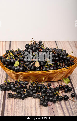 Ripe Aronia berries in a wicker basket on the table. Stock Photo
