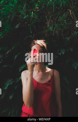 Girls and plants: portrait of a beautiful woman holding a sunlit red leaf. Appreciating, loving nature concept: young female among beautiful green lea Stock Photo