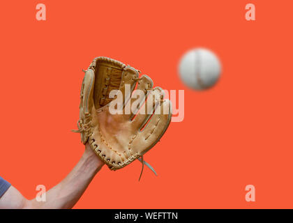 Hand in a leather baseball glove catches a white ball in defocus on a red background Stock Photo