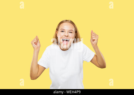 Caucasian young woman's half-length portrait on yellow studio background. Beautiful female model in white shirt. Concept of human emotions, facial expression. Crazy happy, celebrating. Stock Photo