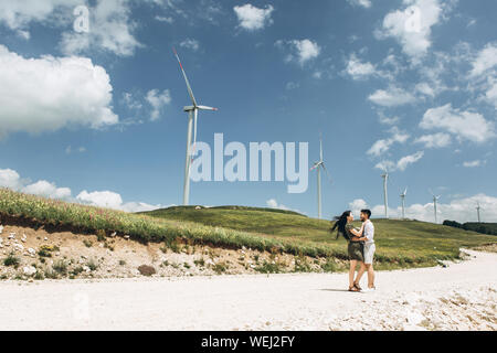 A man hugs a woman against the backdrop of a beautiful natural landscape and windmills. Stock Photo