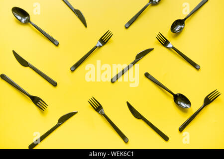 Disposable picnic black knife and forks in diagonal on yellow. Top view. Flat lay. Pattern. Zero waste, save the planet, danger of plastic. Stock Photo