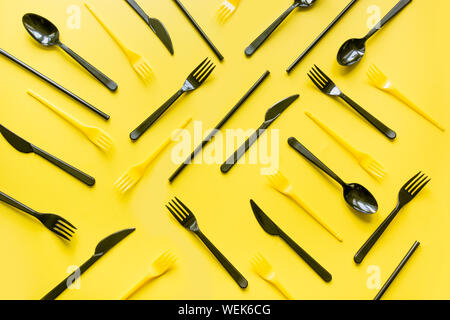 Disposable picnic black knife and forks in diagonal on yellow. Top view. Flat lay. Pattern. Zero waste, save the planet, danger of plastic. Stock Photo