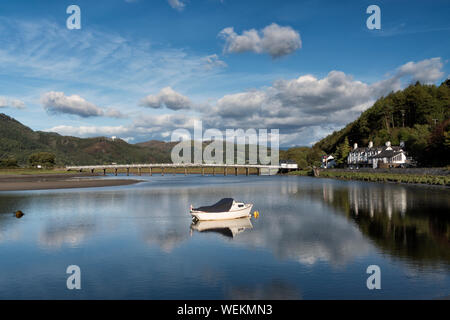 Toll bridge, pool and George 3rd hotel at Penmaenpool in Snowdonia, North Wales. A small boat in moored in the foreground under a blue summer sky. Stock Photo