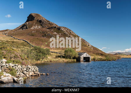View of the boathouse at Cregennan Lakes under a clear blue sky with pointed hill 'Pared y Cefn Hir' in the background. Stock Photo