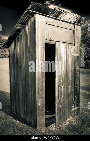 Old,  weathered out-house, or toliet, with door ajar with rusty roof on a hillside field with trees in the Southeastern USA Stock Photo