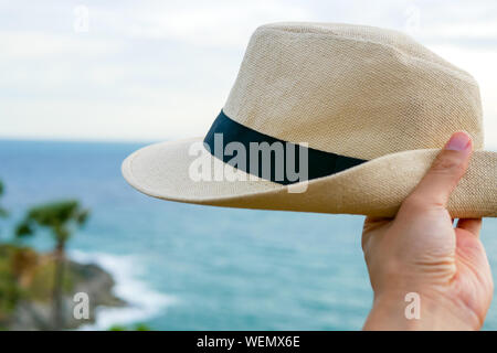 hand is holding panama hat in the blue sea and white sky background that represent relaxing and travel lifestyle Stock Photo