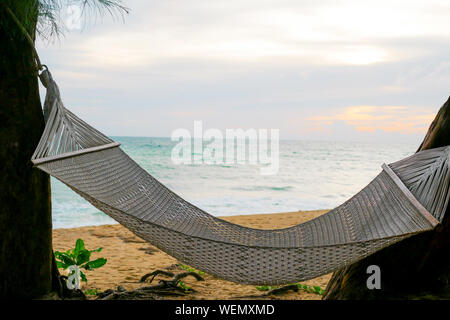 White rope crib is hanging between the trees near the beach and sea in the sunset time that representing relaxing and freshness lifestyle Stock Photo