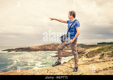 man in casual clothing next to the sea pointing towards the horizon Stock Photo