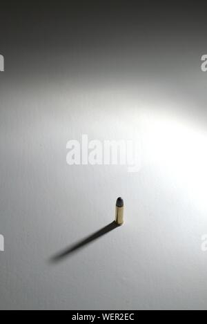 A bullet (.38 lead round nose) standing on a white surface with long dramatic shadow. The background is a gradient to black. Stock Photo