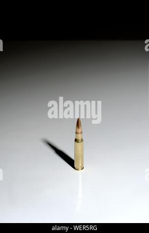 A large bullet (7.62 x 51 mm NATO) standing on a white surface with a gradient to black background. Plenty of negative space. Stock Photo