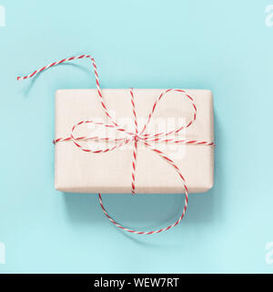 Christmas gift wrapped in white paper with red rope ribbon on blue. Top view and copy space. Square image. Stock Photo
