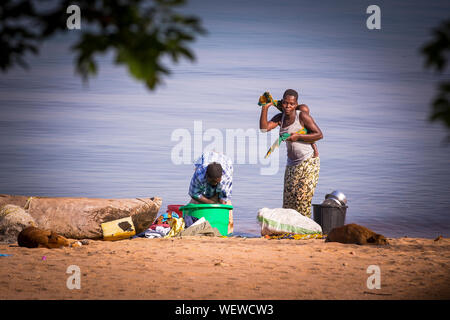 Lake Malawi, Monkey Bay, Woman carry her baby, washing clothes at the Beach, South-East-Africa Stock Photo