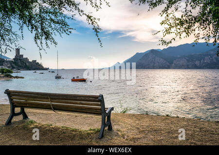 Wooden bench on the shores of Lake garda looking out onto the sunset over the mountains Stock Photo