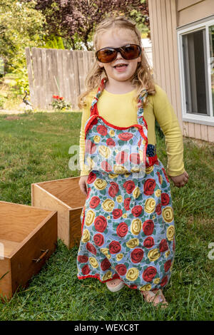 2 year old girl having fun modeling Grandma's sunglasses and apron outside Stock Photo