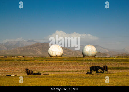 A herd of Kyrgyz horses grazing in front of an abandoned Soviet-era radar station. Antenna globes and Horses on the Silk Road near Kektyube, Kyrgyzstan - Stock Photo
