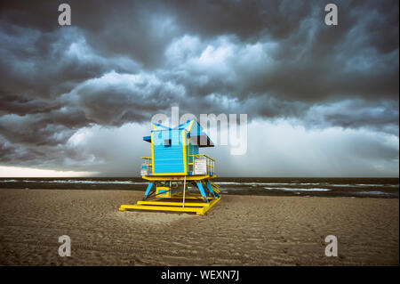 A colorful lifeguard tower is dwarfed by dramatic storm clouds overtaking South Beach in Miami, Florida, USA