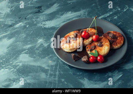 Breakfast Food Tasty Concept. Cheesecakes, cheesecakes, cottage cheese pancakes with cherries and chocolate on a black background concrete table. Clos Stock Photo