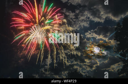 Night fireworks different colors glittering sparkle fireworks on a Nightly sky with large moon and eerie white clouds Stock Photo