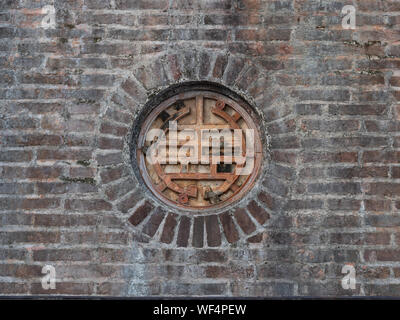 Close up of a metal medallion with geometric design or character set in a brick wall in the Pagoda of the Celestial Lady in Hue Vietnam Stock Photo