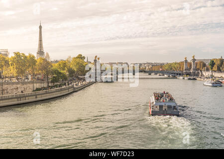 Busy and sunny day in Paris, France with a transportation boat full of tourists riding over the Seine river with the eiffel tower in the left and the Stock Photo