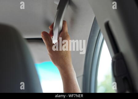 New London, CT / USA - June 22, 2019: Middle aged hands holding on to the grab handle in a casual car
