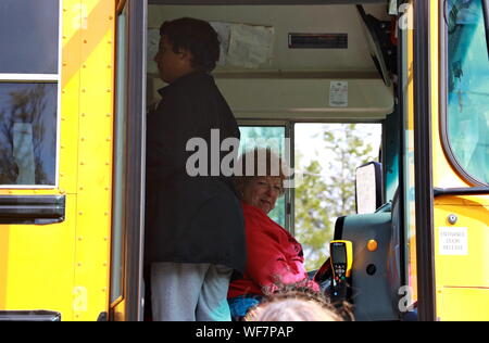 Meriden, CT / USA - April 27, 2019: Caucasian female middle-aged bus driver picking up kids and other passengers Stock Photo