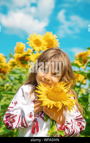 A child in a field of sunflowers in an embroidered shirt. Ukrainian. Selective focus. Stock Photo