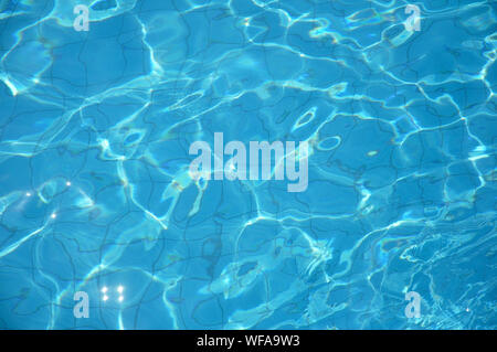 Swimming pool bottom caustics ripple and flow with waves background. Summer background. Texture of water surface. Overhead view. Stock Photo