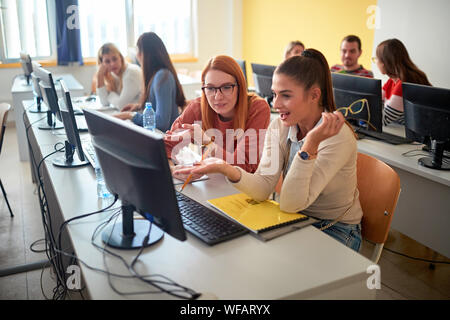 Smiling girl students sitting together at table using computer in class on university Stock Photo