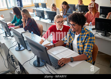 Group of smiling students sitting together at table using computer in class Stock Photo