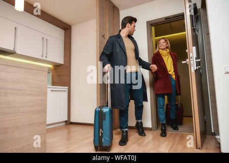 Full-length portrait of young man and woman in casual wear with suitcases entering their room in a hotel. Travelling together concept. Horizontal shot Stock Photo