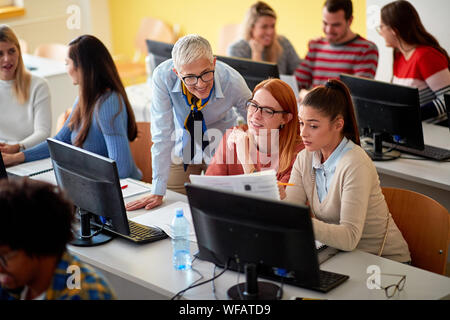 lecturer helping smiling girl students on project on university Stock Photo