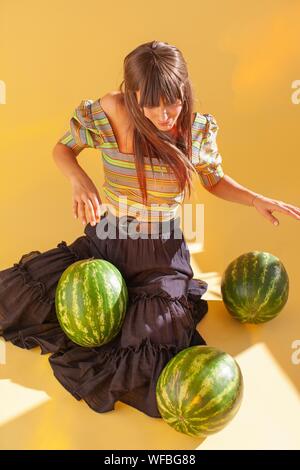 Smiling woman sitting on floor using watermelons as musical drums Stock Photo
