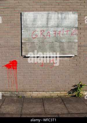 Mis-spelling of the word 'Graffiti' spray-painted on a wall with red paint on a disused factory with a boarded-up window. Stock Photo